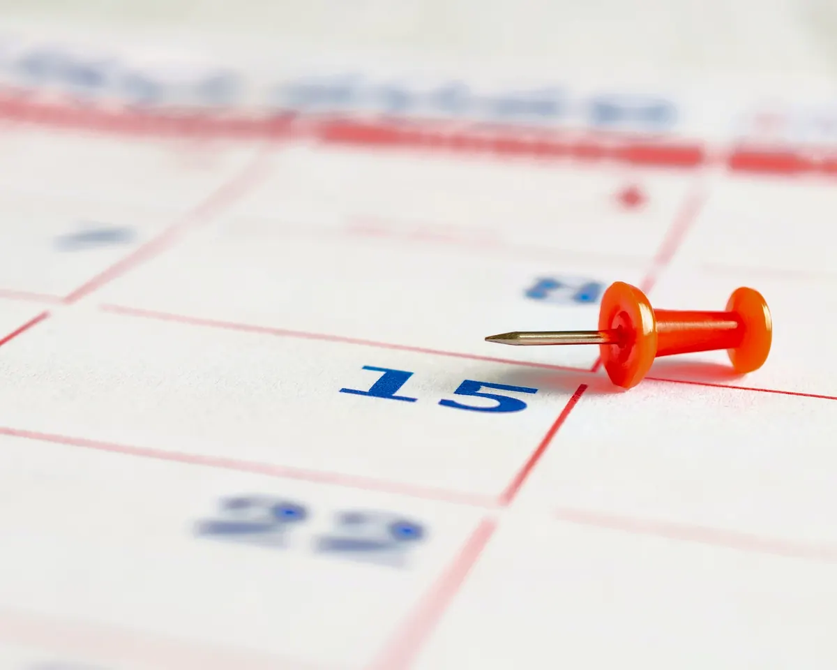A red pin marking the 15th on a paper calendar