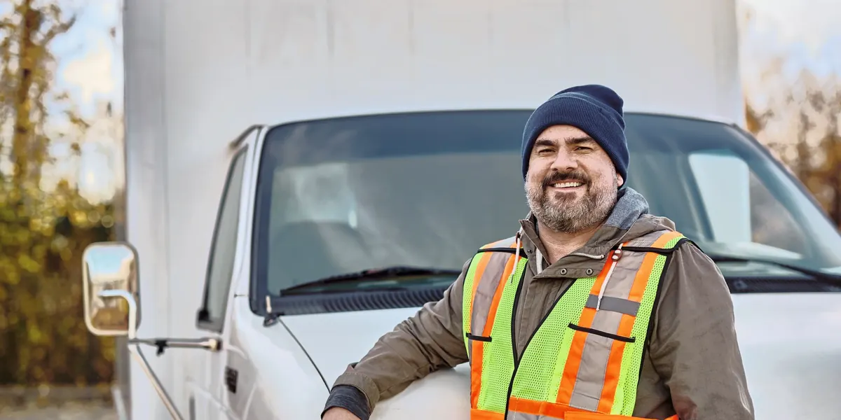 A smiling man in a safety vest leaning on a white work truck