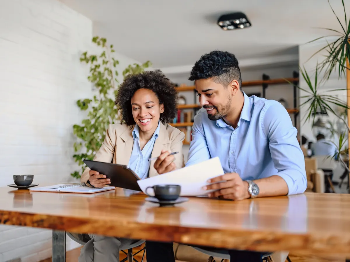 Two people at a wooden table going over a document, one holding a tablet