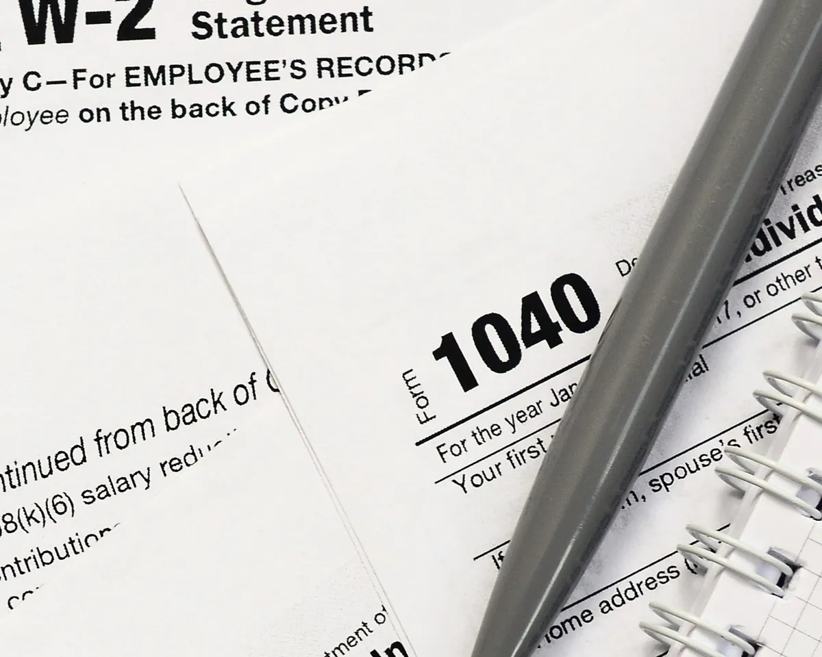 A W-2 and a Form 1040 on a desk, with a pen and a spiral notebook