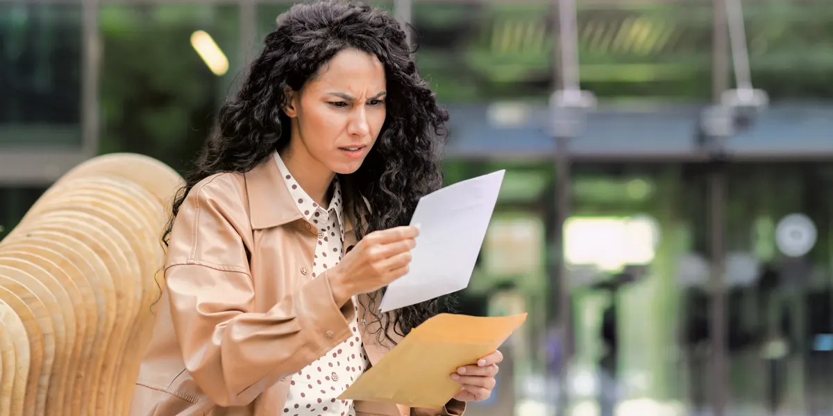 A woman outdoors reading a letter, an envelope in her other hand