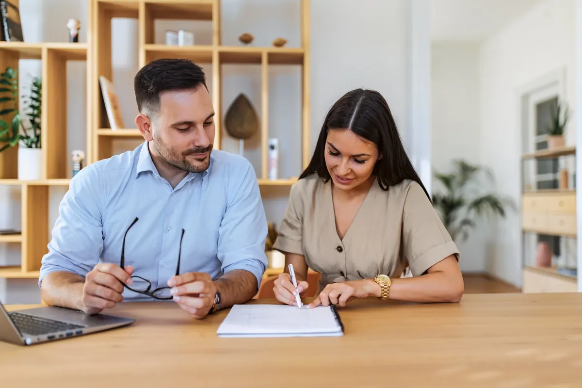 Two people at a table going over notes, with a laptop open beside them