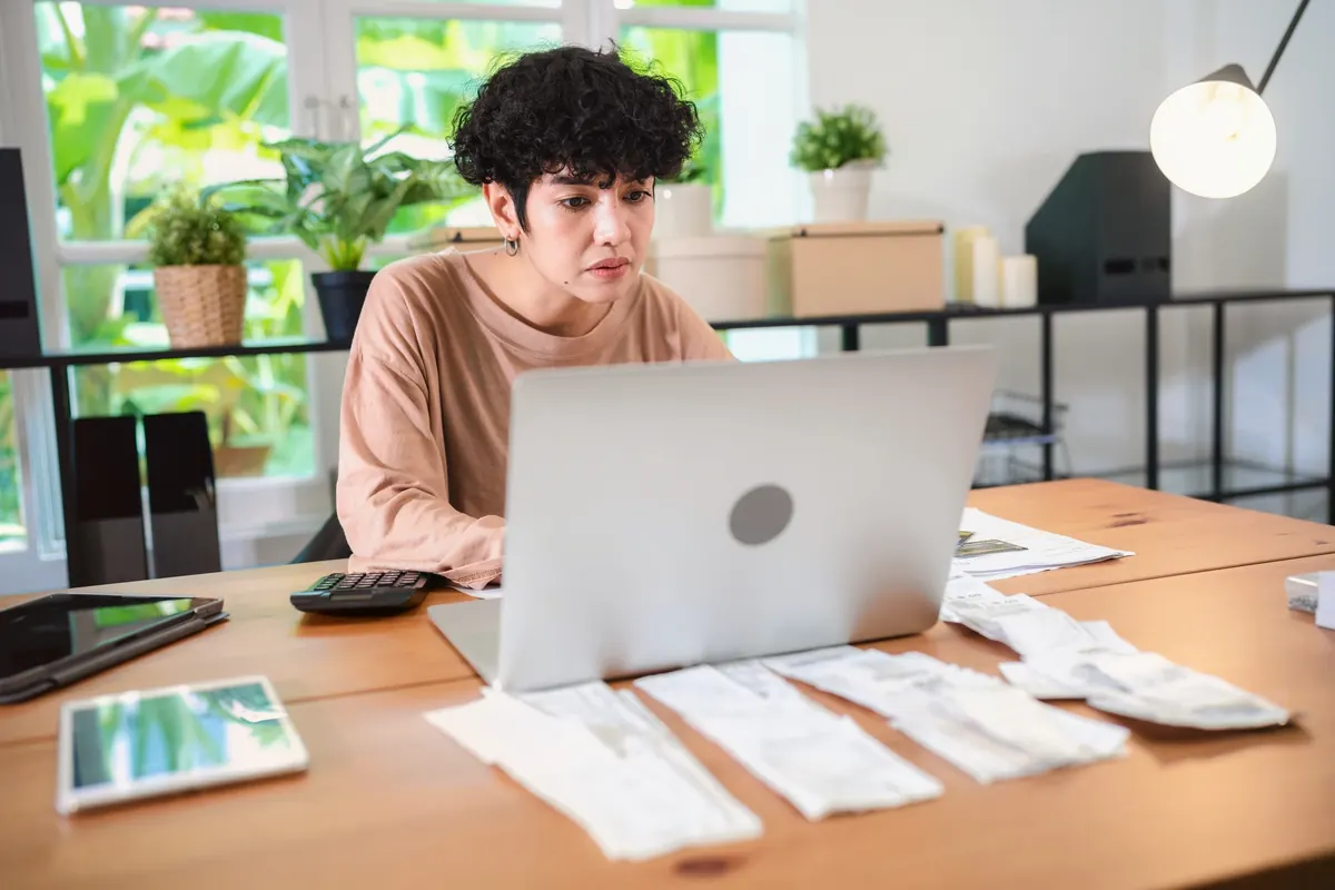 A woman at a desk with a laptop, a calculator and receipts laid out in rows