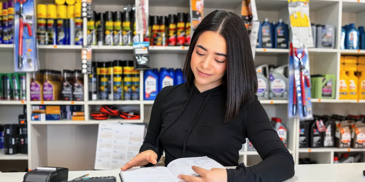 A woman at the counter of an auto parts store, looking over a notebook